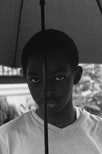 grayscale photo of boy in crew neck shirt holding umbrella