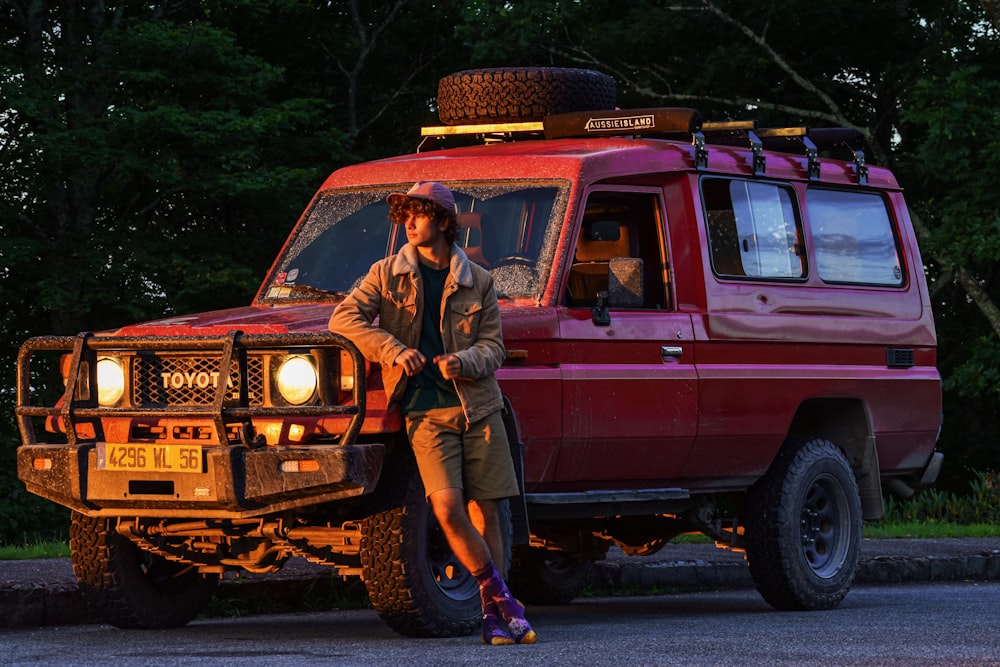 man in brown jacket and brown pants sitting on red suv