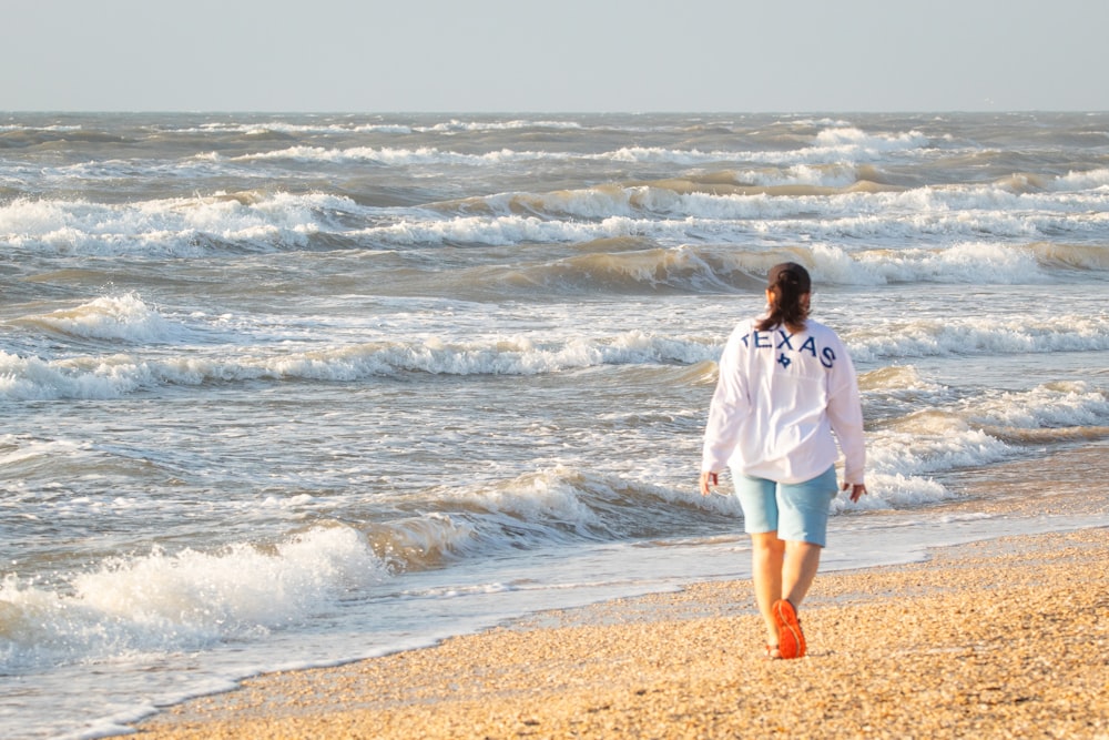 woman in white long sleeve shirt and white shorts standing on seashore during daytime