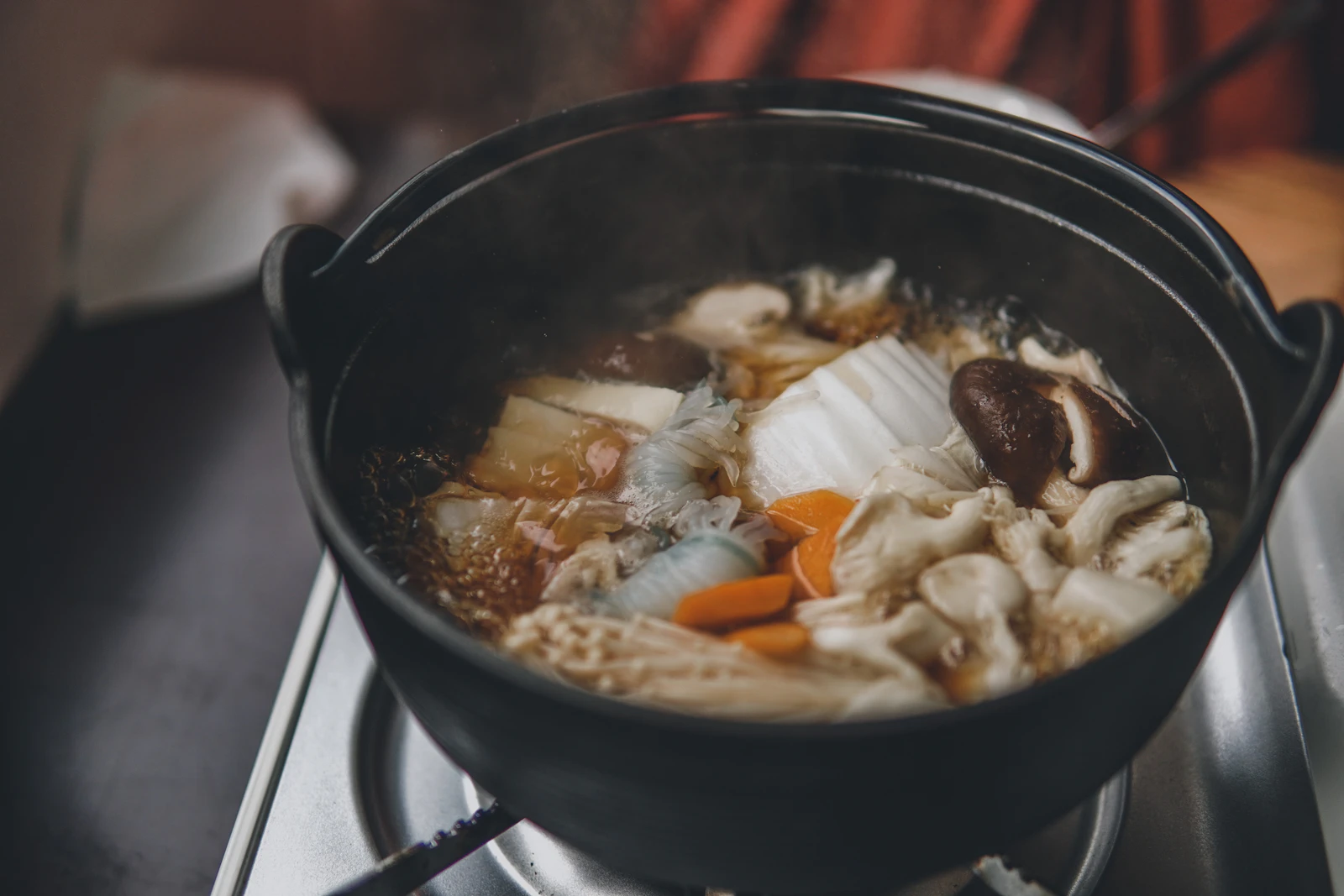 Black cast-iron pot of simmering broth with mushrooms and vegetables on a stove