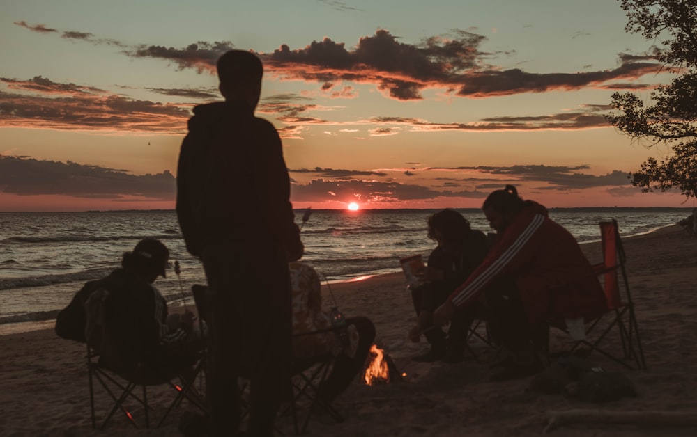 silhouette of people sitting on chair near body of water during sunset