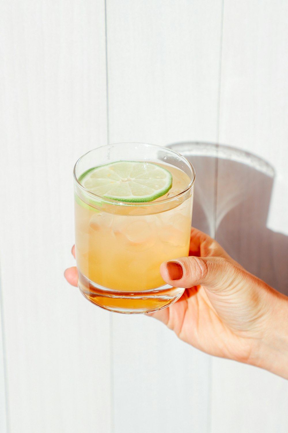 person holding clear drinking glass with yellow liquid