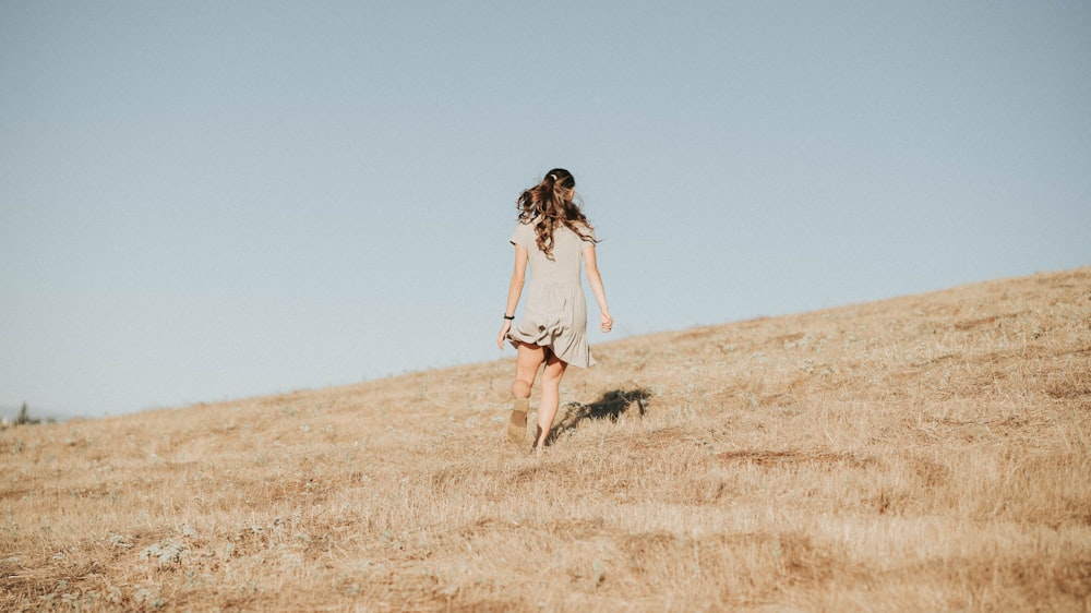 woman in white dress walking on brown grass field during daytime