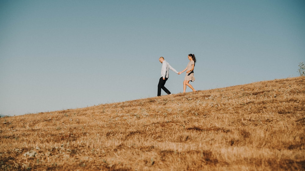 낮에 갈색 잔디밭을 걷는 동안 손을 잡고 있는 남자와 여자