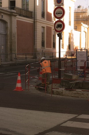 man in orange jacket standing near red and white traffic light during daytime