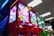 A row of vibrant claw machines line an indoor arcade, each adorned with brightly lit displays and priced at 50 cents. The foreground machine is predominantly red, with others in different colors, all under fluorescent ceiling lights.