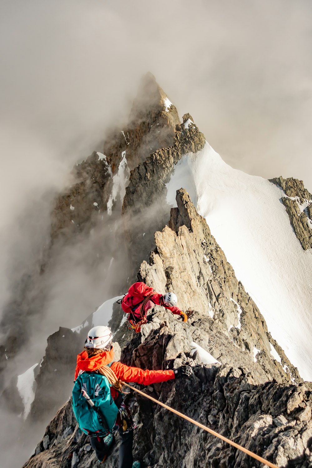 Personne en veste rouge et pantalon bleu assise sur une montagne rocheuse couverte de neige pendant la journée