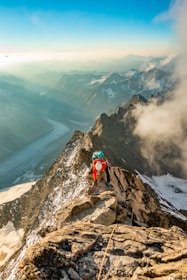 A climber ascending a rugged alpine ridge under a clear blue sky.