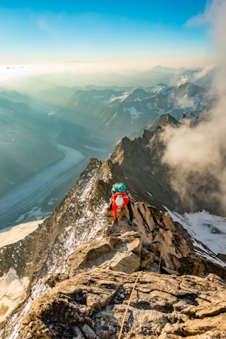 A climber reaching the summit of a snowy mountain under a clear blue sky.