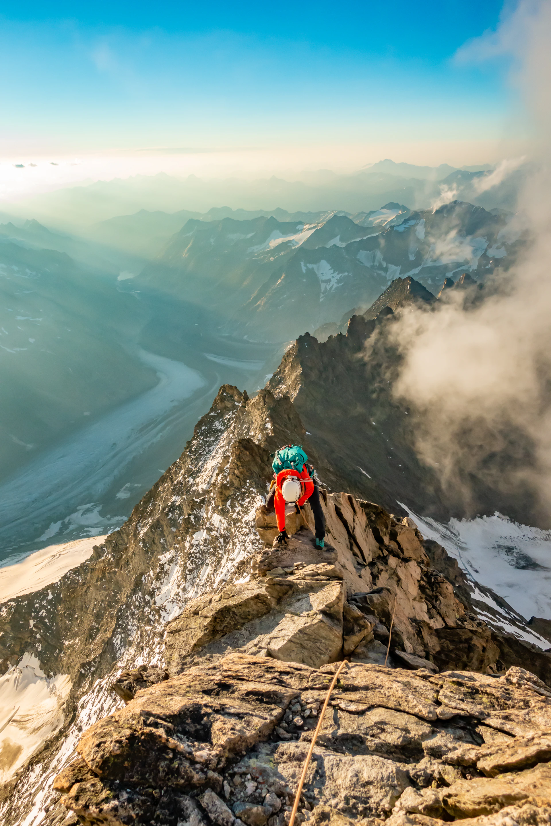 A daring climber scaling a jagged cliff at sunrise, with a vast mountain range stretching into the distance.