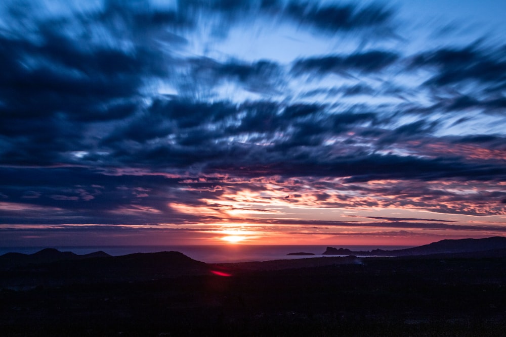 silhouette of mountains under cloudy sky during sunset