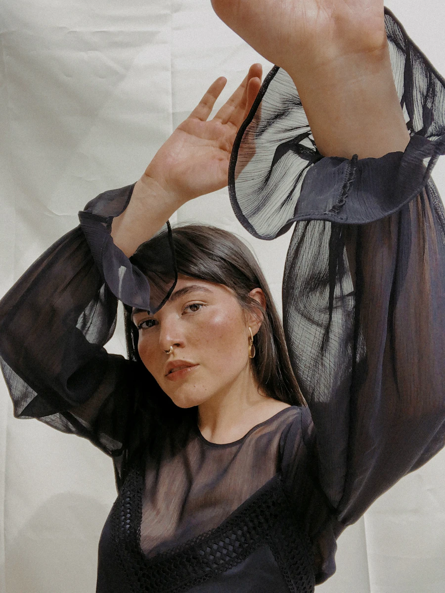 Woman in a black organza blouse raising a voluminous sheer sleeve