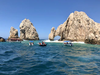 Travelers aboard an outrigger boat laughing and pointing towards dramatic rock formations jutting out from the sea