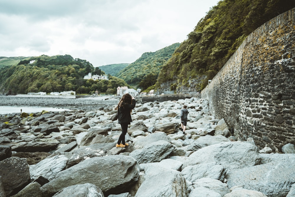 man in black jacket and yellow pants standing on rocky river during daytime