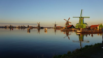 brown wooden windmill on green grass field near body of water during daytime