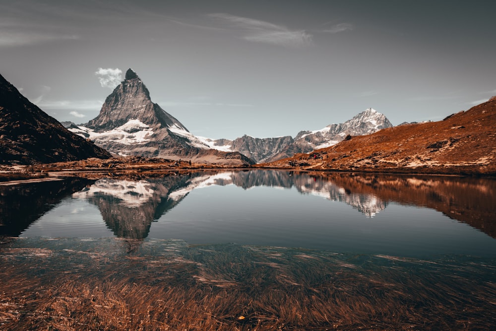 snow covered mountain near lake under cloudy sky during daytime