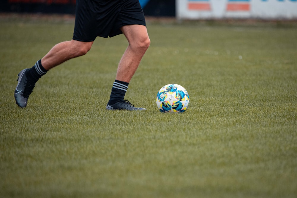 man in black shorts and white and blue soccer ball on green grass field during daytime