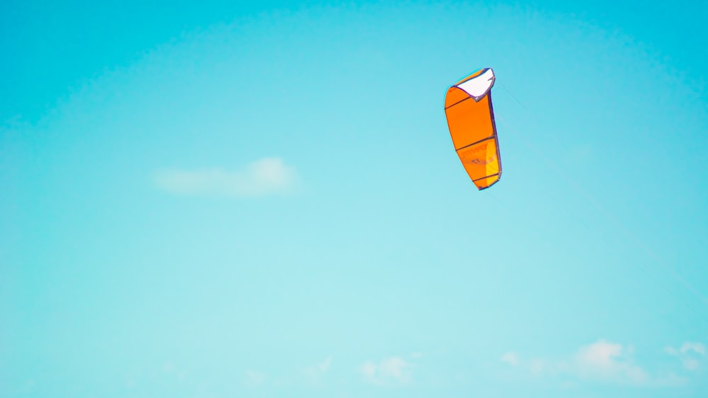 orange and white kite flying under blue sky during daytime