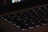 Close-up of a laptop keyboard with backlit keys in a dim room.