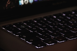 Close-up of a notebook keyboard with backlit keys glowing softly in a dim room.