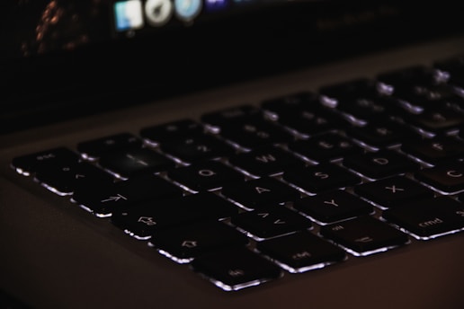 Close-up of a sleek laptop keyboard with glowing keys in a dimly lit room.