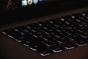 Close-up of a laptop keyboard with backlit keys in a dim room.