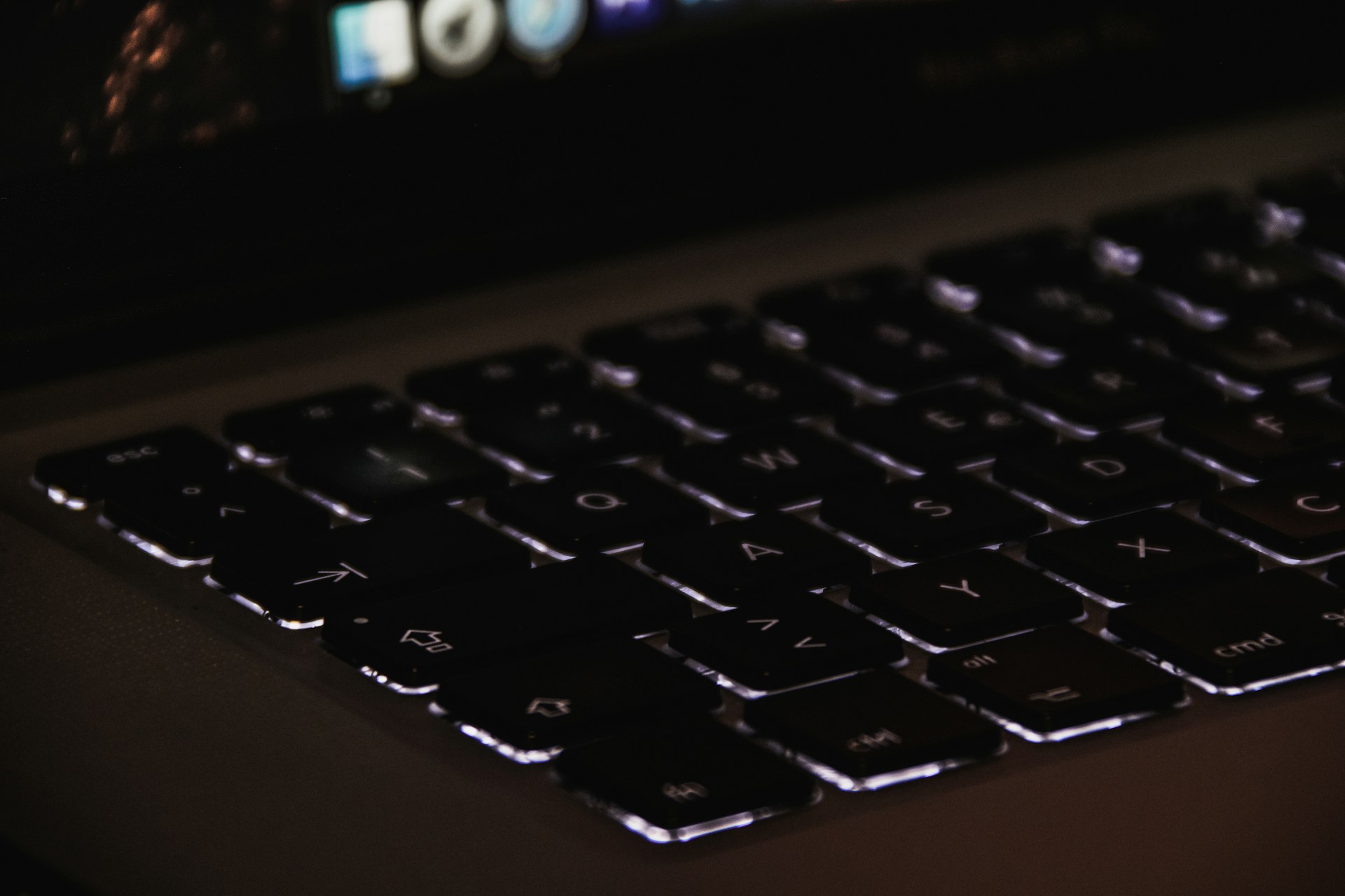Close-up of a laptop keyboard with backlit keys glowing in a cozy, dimly lit room.