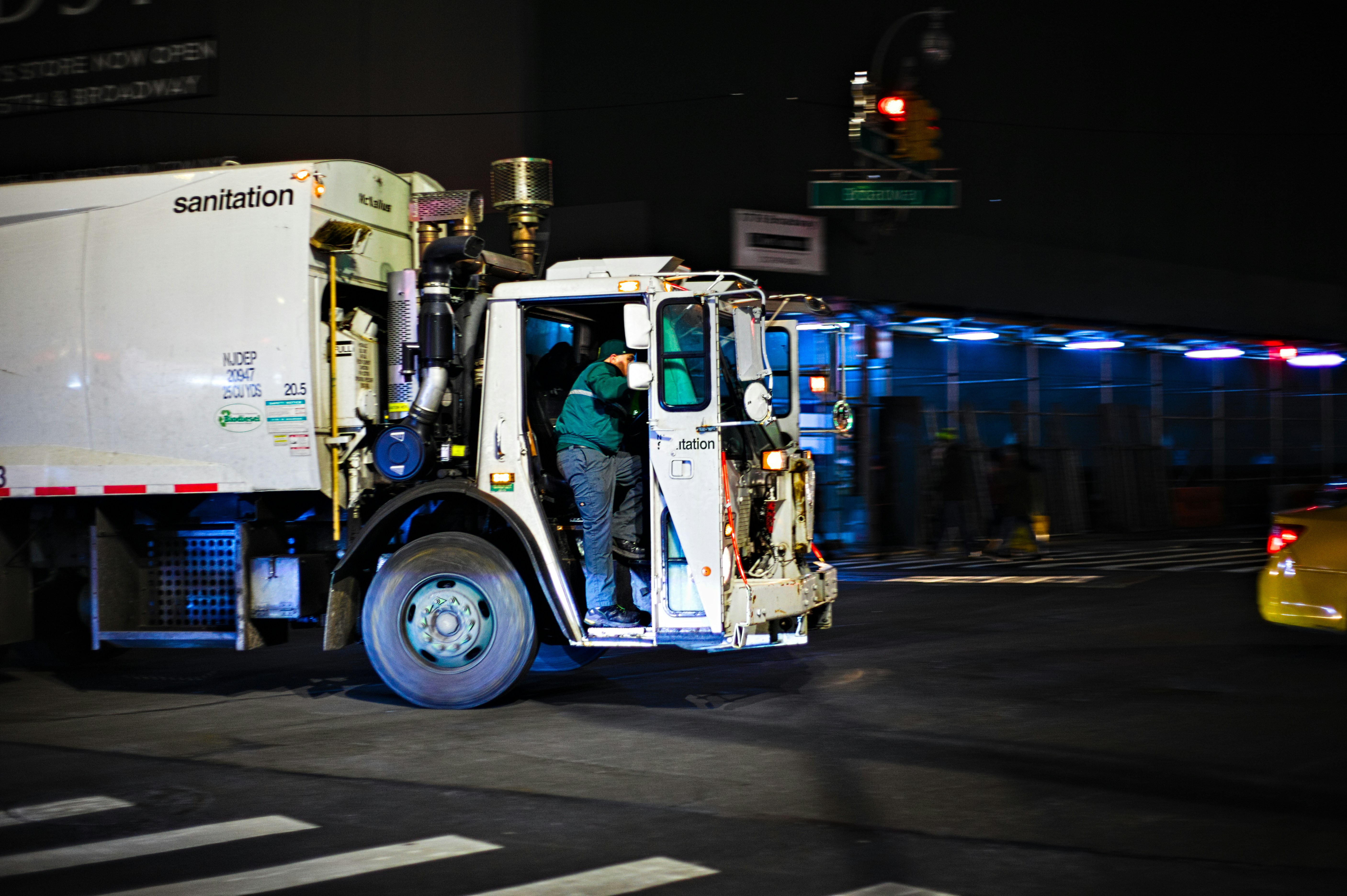 A New York City Sanitation Department garbage truck turning onto Broadway on an evening in late December.