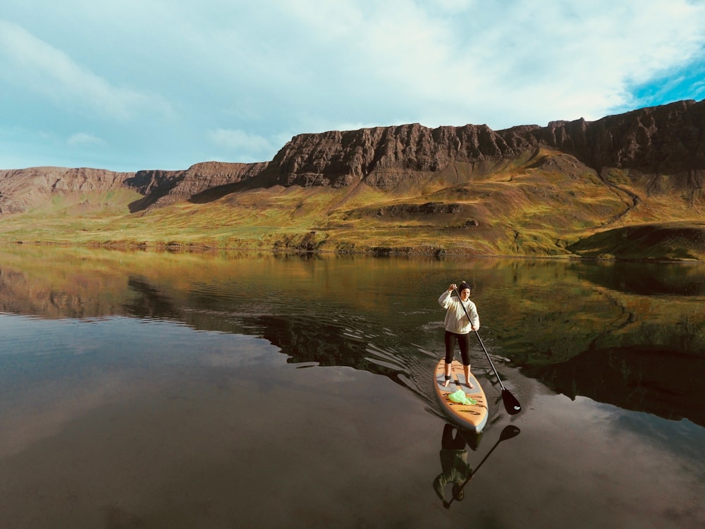 man in black shorts and black shirt sitting on rock formation near lake during daytime