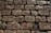 A surface made up of unevenly arranged cobblestones, with dirt and some fallen leaves scattered across it. The stones are weathered, showing signs of age and wear, with a rough texture and varying shades of gray and brown.
