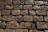 A surface made up of unevenly arranged cobblestones, with dirt and some fallen leaves scattered across it. The stones are weathered, showing signs of age and wear, with a rough texture and varying shades of gray and brown.
