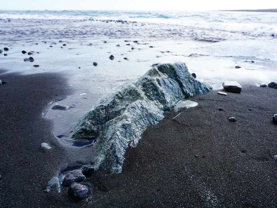 Large jagged rock formation dominates rocky beach with scattered smaller rocks nearby always