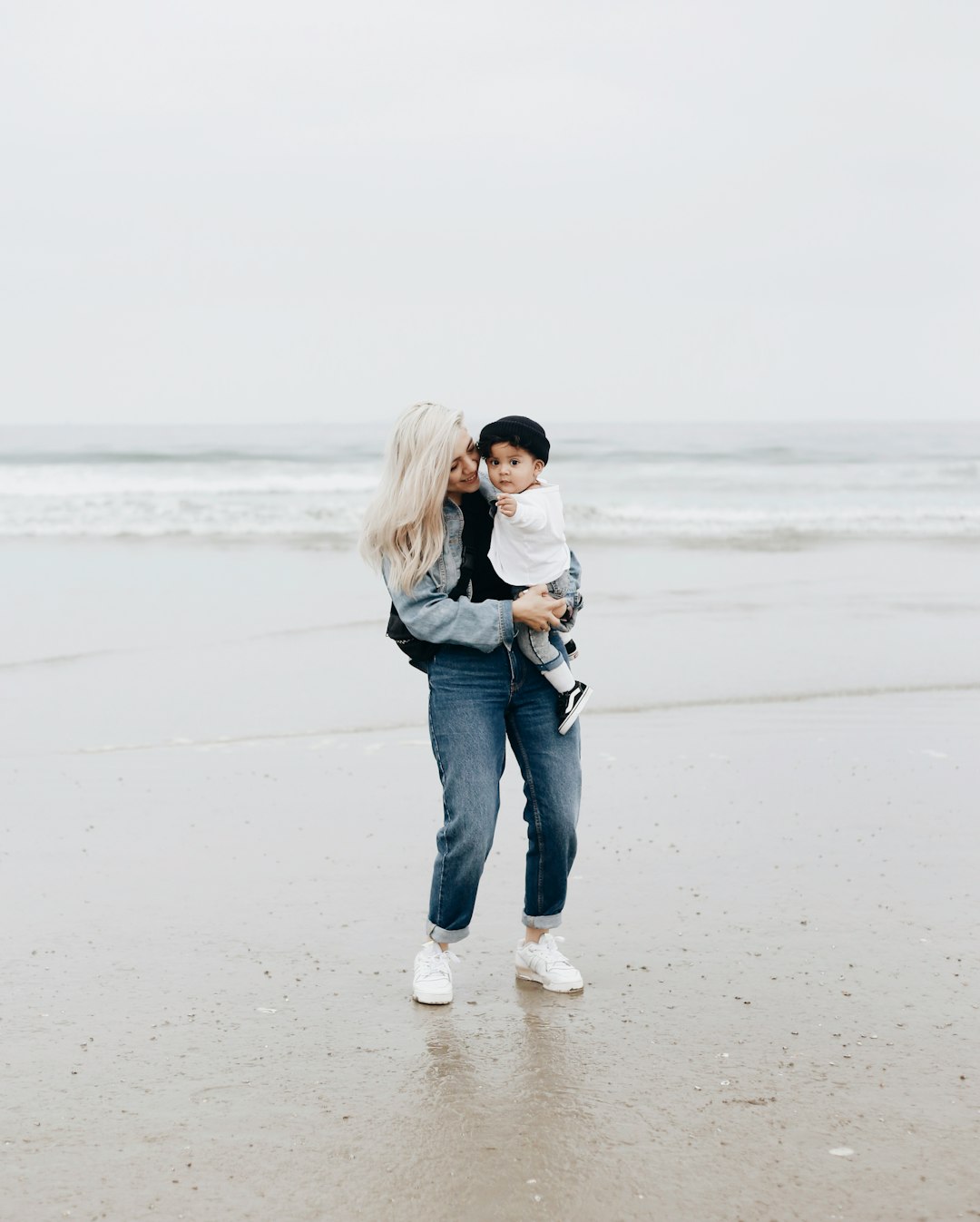 woman in black jacket and blue denim jeans standing on beach during daytime