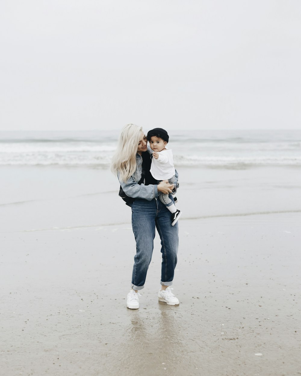 Frau in schwarzer Jacke und blauer Jeans tagsüber am Strand