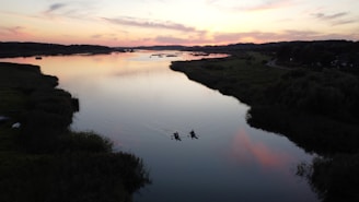 A serene riverside scene with locals kayaking and birds flying overhead at dusk