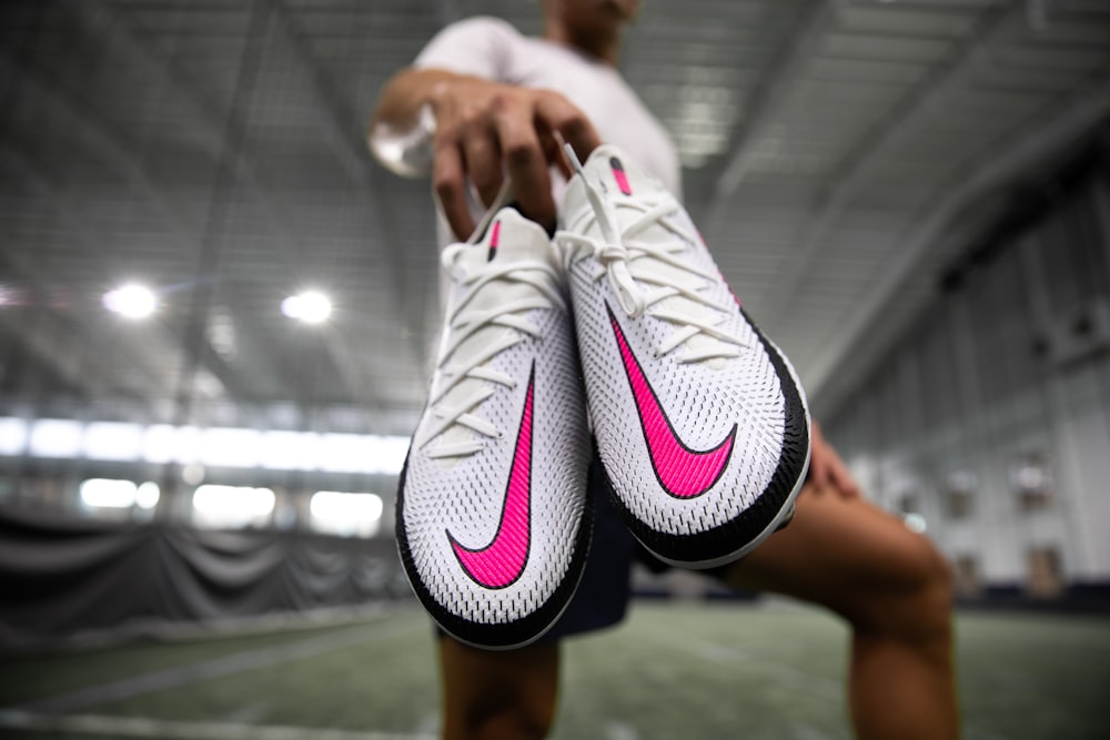 person holding white and pink nike athletic shoes