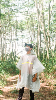 A rugged explorer wearing a high-denier ripstop poncho standing on a rain-soaked trail surrounded by dense forest.