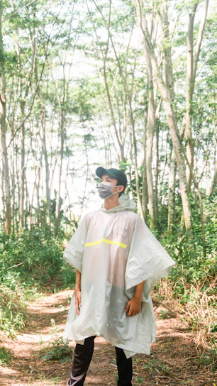 A rugged explorer wearing a high-denier ripstop poncho standing on a rain-soaked trail surrounded by dense forest.