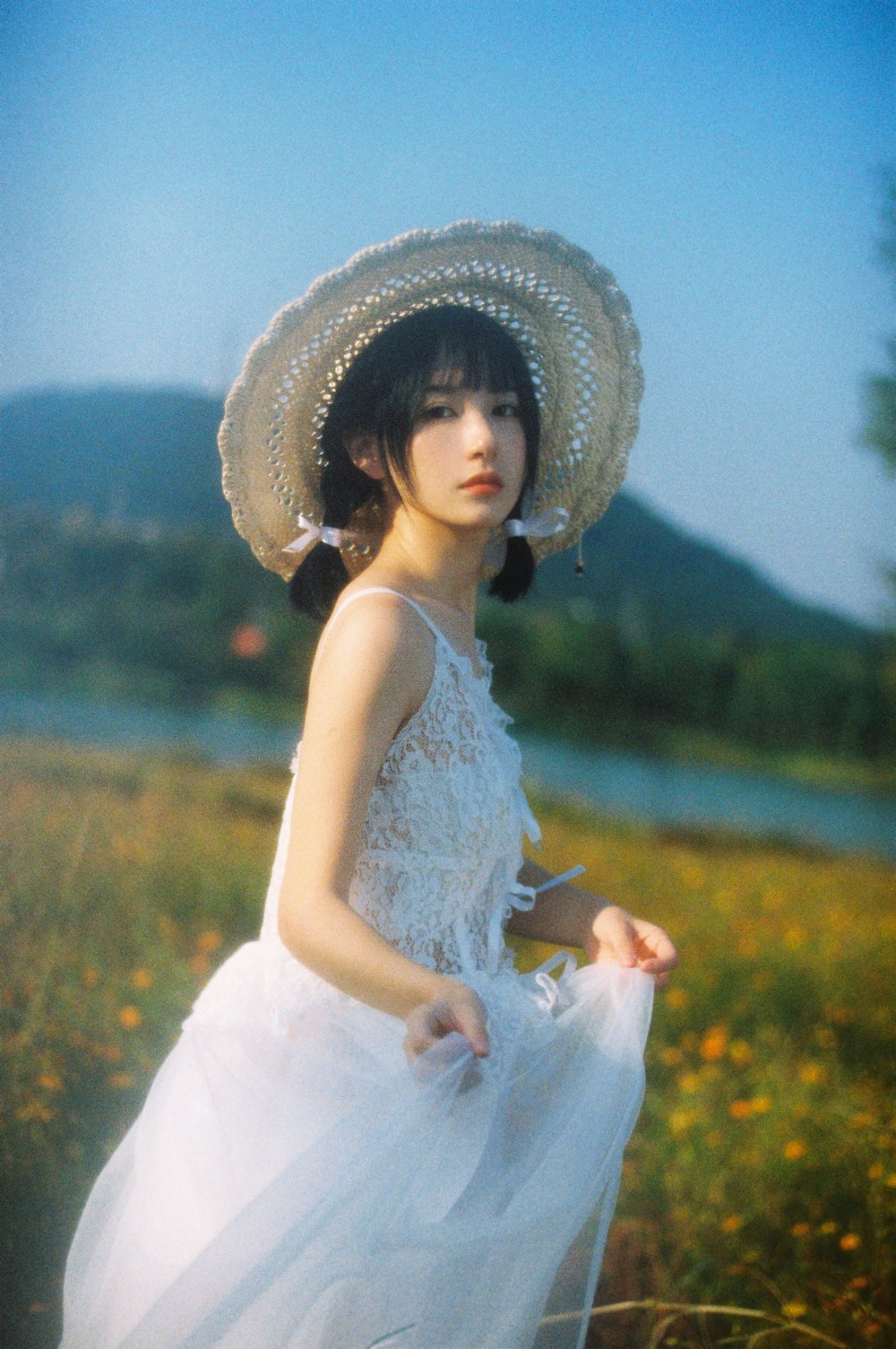 Mujer en vestido blanco sin mangas con sombrero blanco para el sol de pie en el campo de hierba verde durante el día