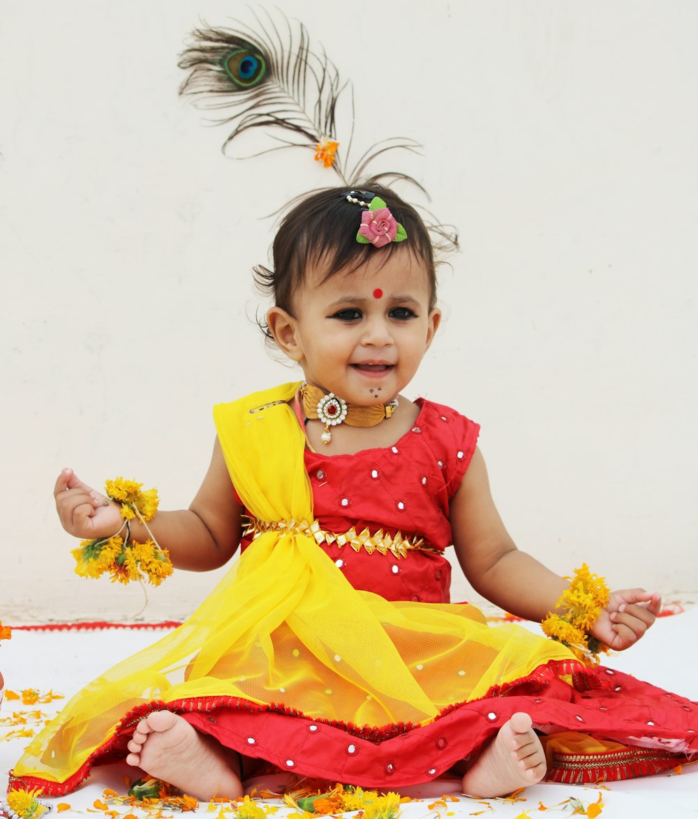 girl in red and yellow dress sitting on white and red floral textile