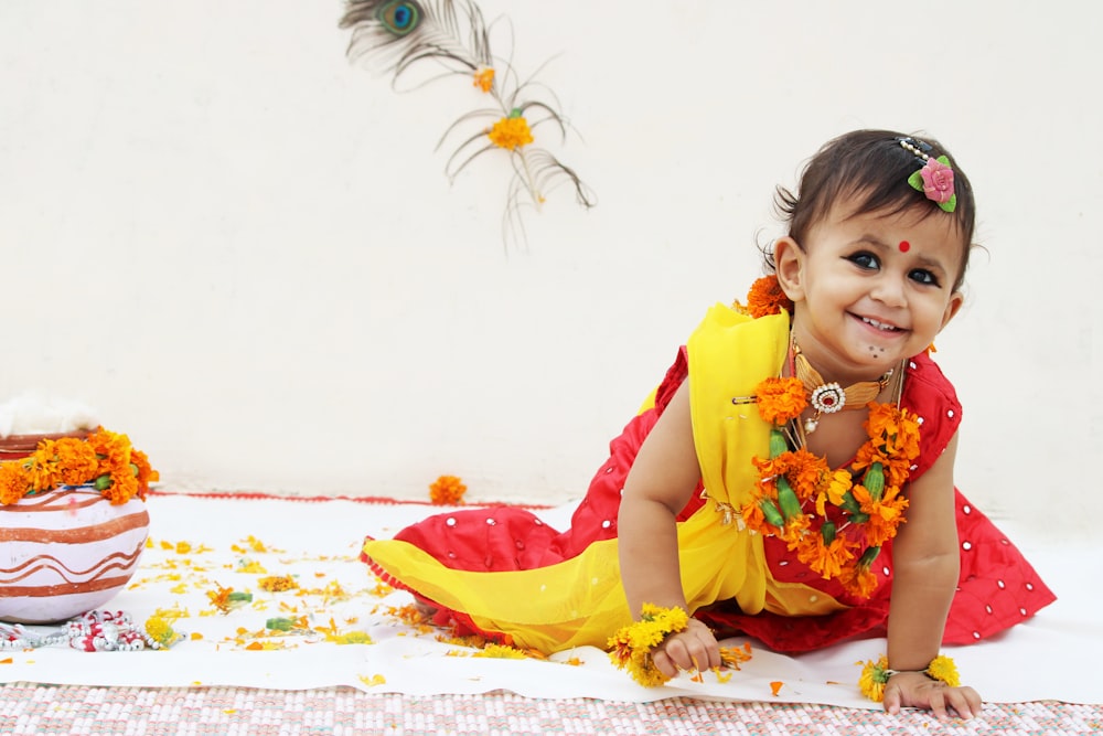 girl in yellow and red dress sitting on white and blue floral textile