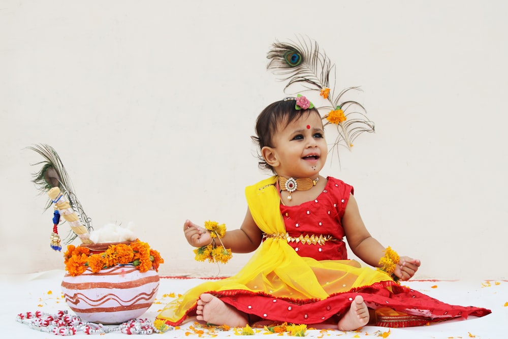 girl in yellow and red dress sitting on white and pink floral textile