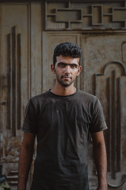 man in black crew neck t-shirt standing near brown wooden wall in Ahvaz Iran