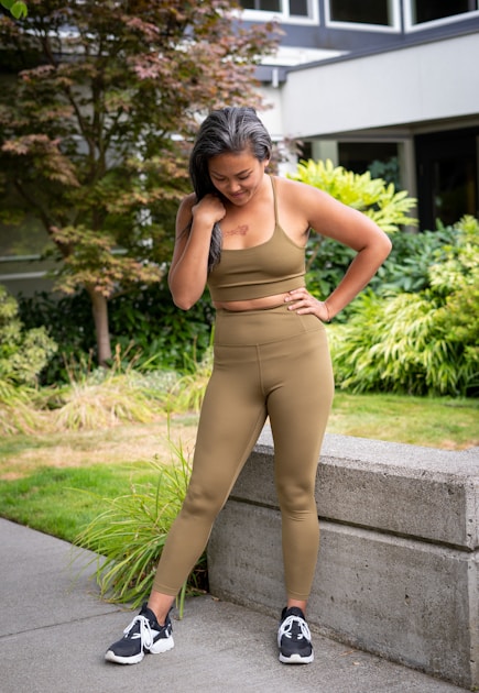 Woman in a matching olive sports bra and high-rise leggings standing in a garden