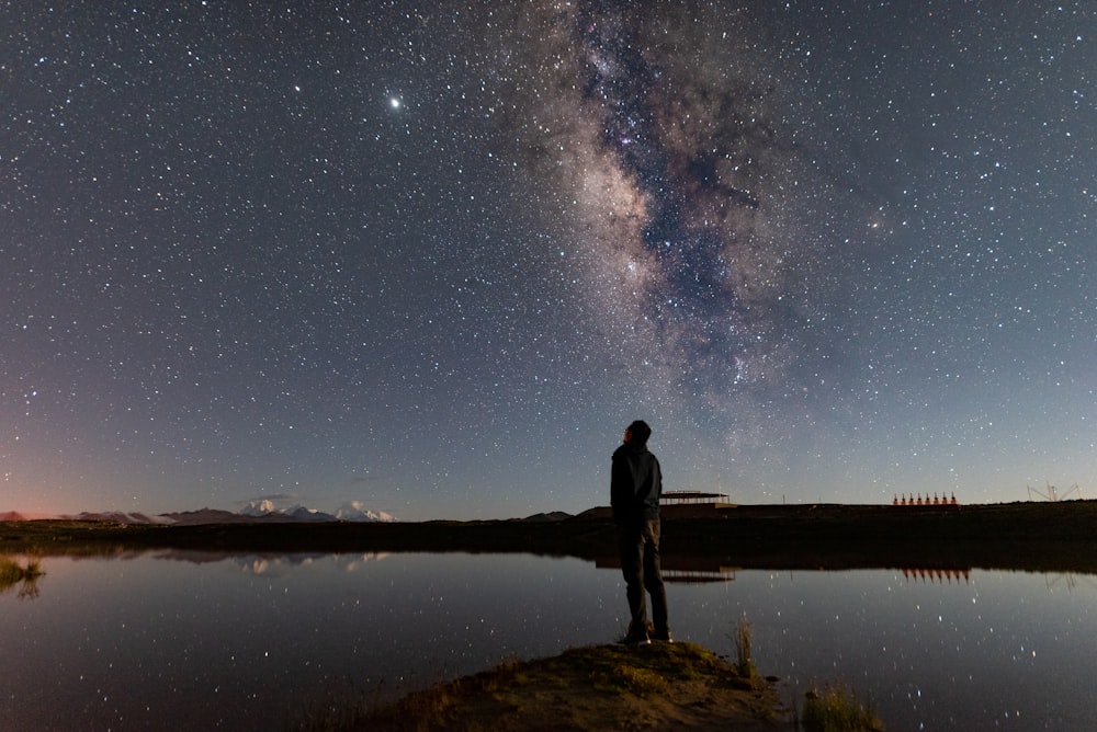man standing on brown rock near body of water during night time