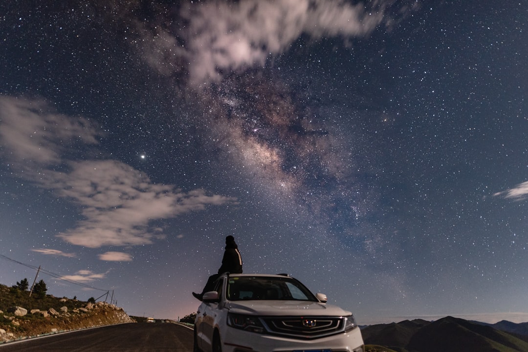 man sitting on white car under starry night