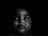 A baby is captured in a low light setting, creating a dramatic contrast with its facial features highlighted against a dark background.