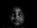 A baby is captured in a low light setting, creating a dramatic contrast with its facial features highlighted against a dark background.