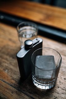 A close-up of a sleek stainless steel flask resting on a wooden picnic table with morning dew.