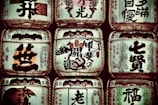 Several traditional sake barrels are stacked in a symmetrical arrangement. Each barrel is adorned with Japanese calligraphy and symbols, highlighting intricate designs and various insignias representative of sake breweries.